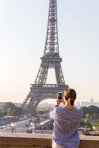 美しい女の子はパリ、フランスの有名なエッフェル塔のスマートフォンで写真を撮ります. - 写真・画像