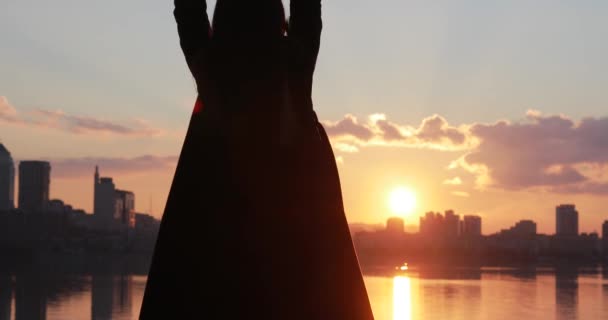 Silhouette of woman with raised hands looking at cityscape sunrise - Πλάνα, βίντεο