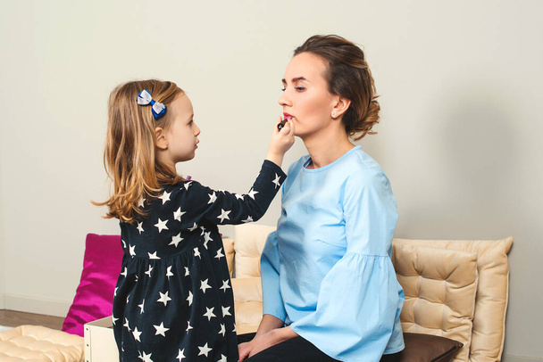 Happy loving family. Mother and daughter are doing makeup. Lovely mom and child having fun together. Daughter applying lipstick on her mom's lips. Mother's Day. Healthy kid cosmetics. - Foto, immagini