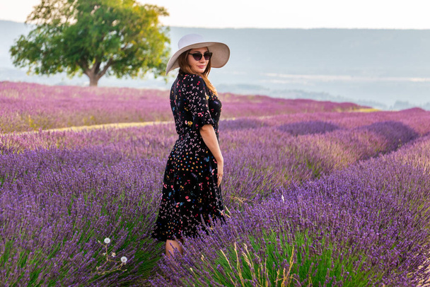 Girl in a dress with flowers and big white hat in the lavender fields in Provence, Valensole, France. Picturesque summer nature landscape and agriculture area. Popular travel destination. - Photo, Image