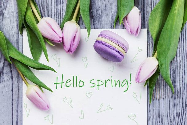 Bonjour carte de printemps. Tulipes fleurs rose printemps, macaron violet et drap blanc sur fond bois gris. Vue du dessus
 - Photo, image