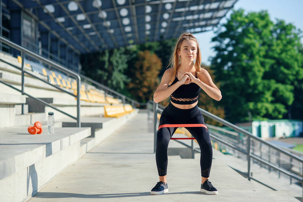 Young sporty woman doing exercises with rubber band outdoor - Photo, Image
