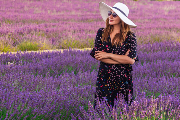 Girl in a dress with flowers and big white hat in the lavender fields in Provence, Valensole, France. Picturesque summer nature landscape and agriculture area. Popular travel destination. - Foto, Imagem