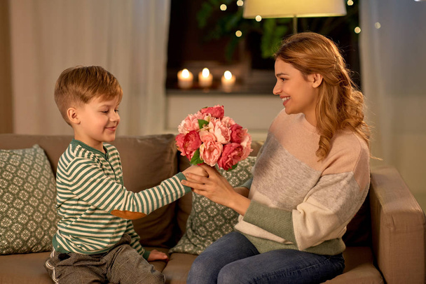smiling little son gives flowers to mother at home - Zdjęcie, obraz