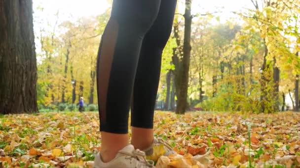4k video of camera slowly moving from feet to head of sporty young woman drinking water from botttle after doing sports and fitness exercise at autumn park - Felvétel, videó