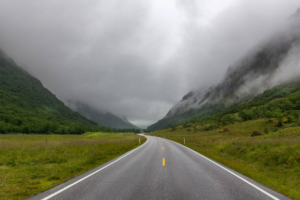 The road leading a mysterious valley surrounded by clouds of the Norwegian mountains. - Zdjęcie, obraz