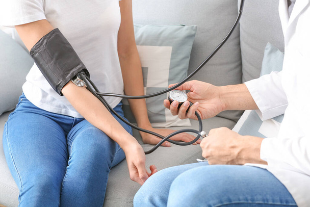 Doctor measuring blood pressure of young woman at home - Foto, afbeelding