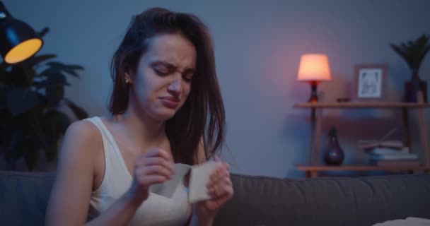 Close up of young unhappy woman tearing angrily photo and throwing away while sitting on sofa. Sad girl crying and putting hand on face after painful brokeup with lover. - Séquence, vidéo