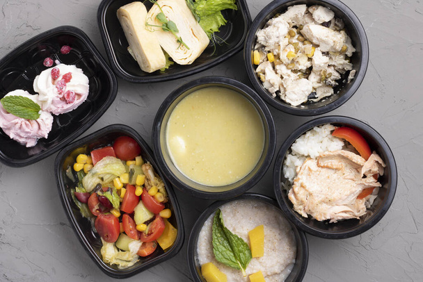 Healthy business lunch containers at workplace. Cream soup with quail eggs, vegetables and fried chicken lunch box on grey table, top view - Photo, Image