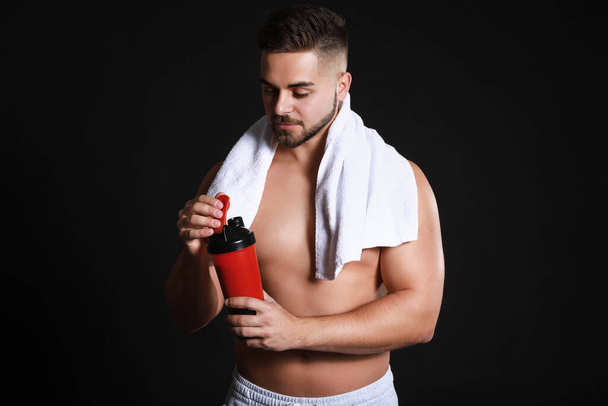 Sporty man with protein shake on dark background - Photo, Image