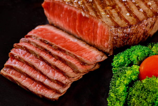 Dilimlenmiş az pişmiş sığır filetosu brokoli ile ahşap masada siyah arka planda. - Fotoğraf, Görsel
