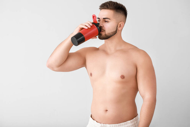 Sporty man with protein shake on light background - Foto, Imagen