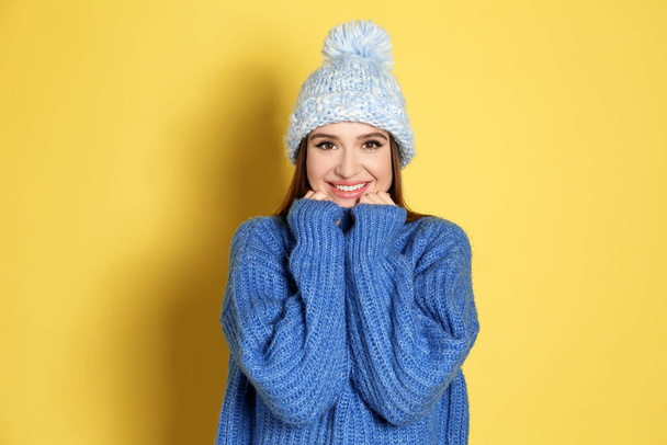 Young woman wearing warm sweater and hat on yellow background. Winter season - Foto, Imagem