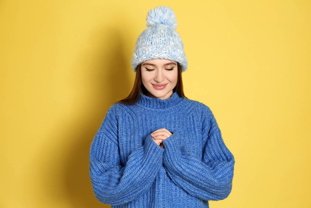 Young woman wearing warm sweater and hat on yellow background. Winter season - Фото, изображение