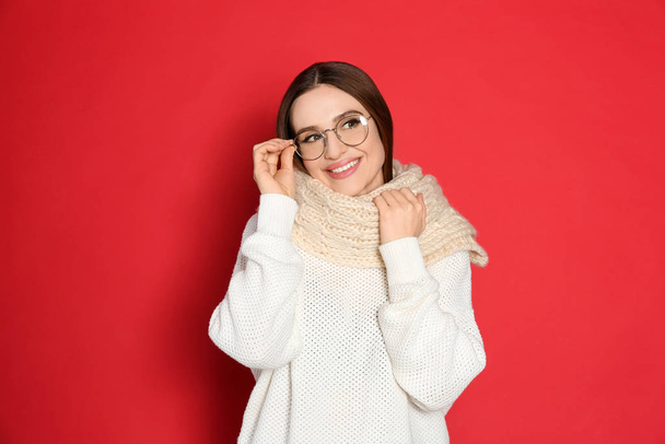 Young woman wearing warm sweater and scarf on red background. Winter season - Foto, afbeelding