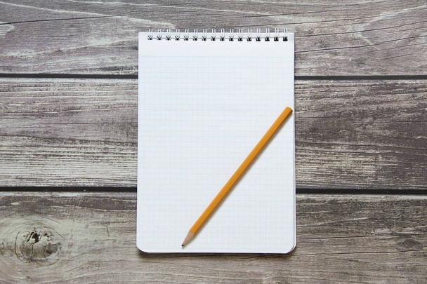 Notepad with a blank white sheet in a checker paper with simple graphite pencil lies on the background of wooden boards - Foto, imagen