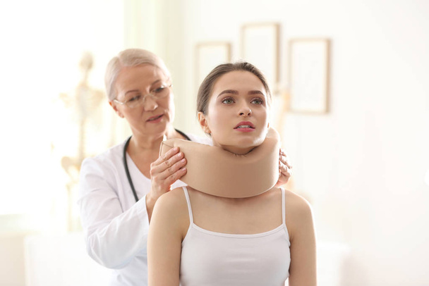 Female orthopedist applying cervical collar onto patient's neck in clinic - Фото, изображение