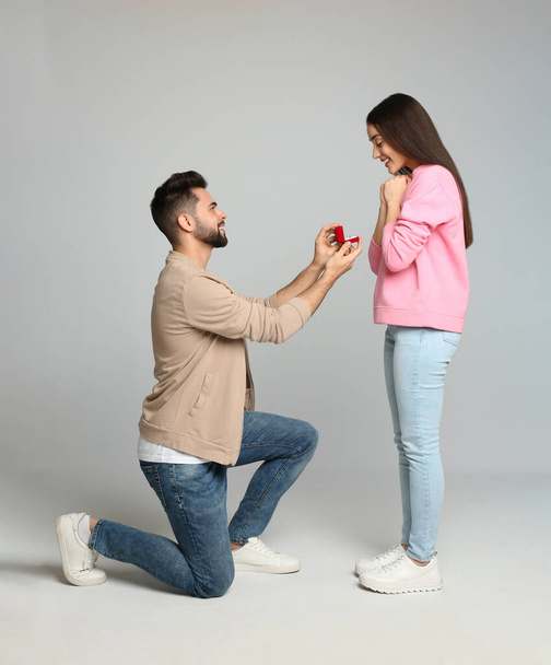 Man with engagement ring making marriage proposal to girlfriend on light grey background - Foto, imagen