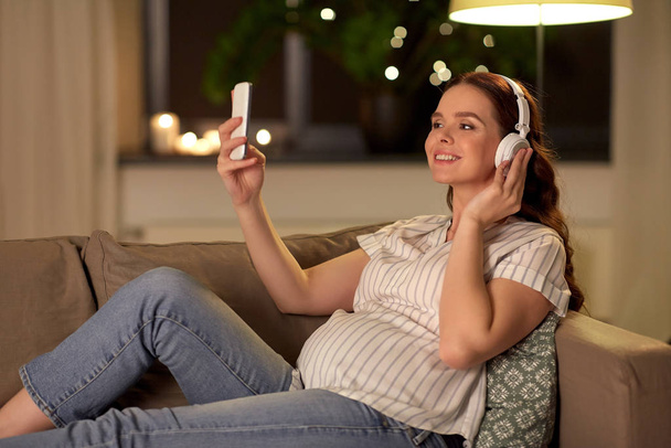Těhotná žena s chytrým telefonem a sluchátky - Fotografie, Obrázek