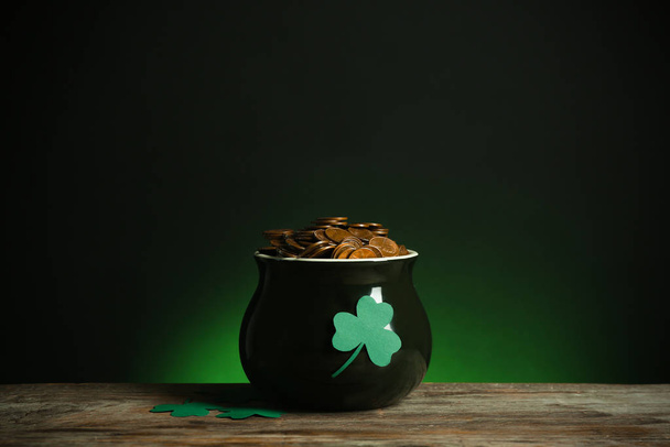Pot with gold coins and clover on wooden table against dark background. St. Patrick's Day - Foto, afbeelding