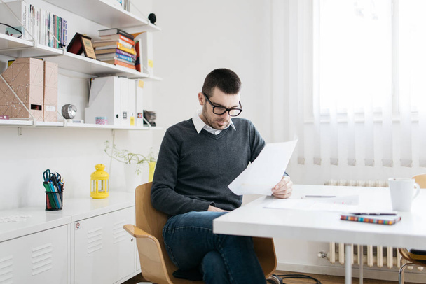 Концентрированный сотрудник читает бумажный лист в офисе
 - Фото, изображение