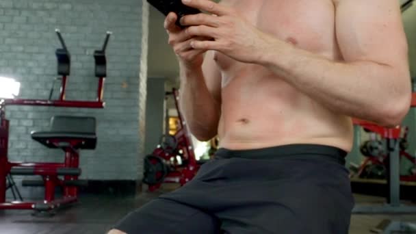 Focused Shot of Man Toned Abs as He's Using His Phone in Between Gym Exercises - Felvétel, videó