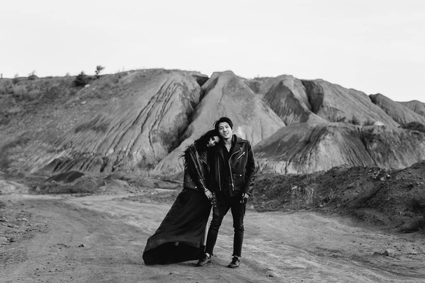 An Asian couple in love in black leather clothes walk in nature among the trees. Black-white - Zdjęcie, obraz