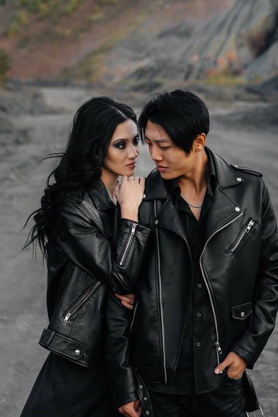An Asian couple in love in black leather clothes walk in nature among the trees. Style, fashion, love - 写真・画像