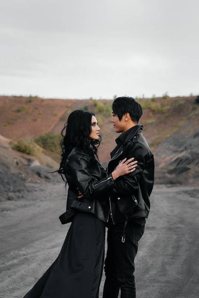 An Asian couple in love in black leather clothes walk in nature among the trees. Style, fashion, love - Photo, Image