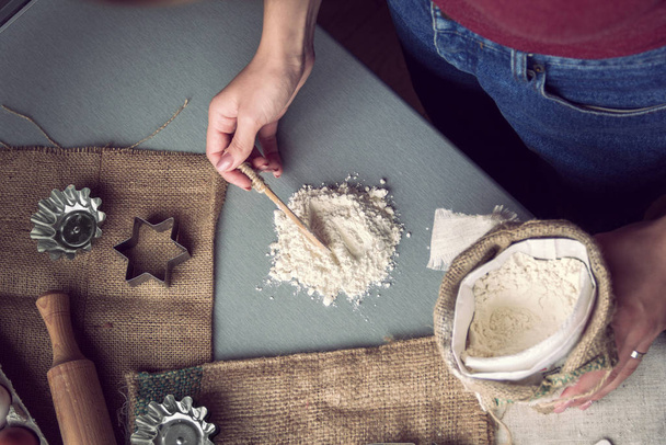 Las manos femeninas recogen la harina con la cuchara para la preparación de las galletas
 - Foto, imagen