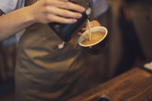 Closeup cup of coffee with pouring milk in a female barista hands - Fotoğraf, Görsel