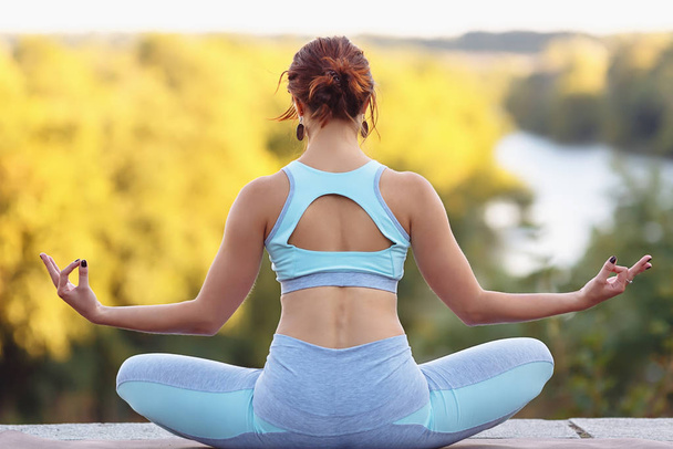 Pretty young sexy woman doing yoga exercises in the park on blurry background - Photo, Image