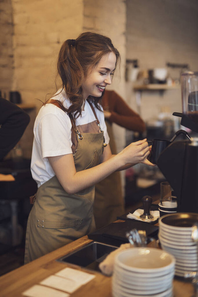 Young and cheerful barista woman make a coffee in the cafeteria - Fotó, kép