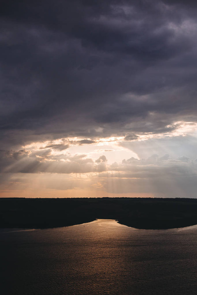 Bella vista dei raggi del sole dalle nuvole scure sopra il lago. Luce del tramonto sul paesaggio collinare e fluviale. Paesaggio drammatico e lunatico. Lago Bakota e fiume Dniester in Ucraina
 - Foto, immagini
