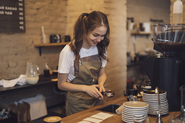 Young and cheerful barista woman make a coffee in the cafeteria - 写真・画像