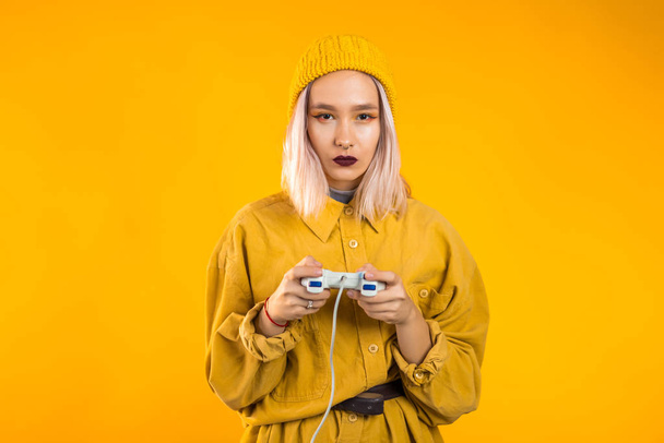 Pretty young girl playing video exciting game on Tv with joystick on yellow studio wall. Using modern technology. - Foto, Imagen