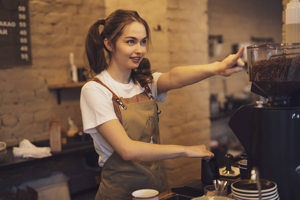Young and cheerful barista woman make a coffee in the cafeteria - Fotó, kép