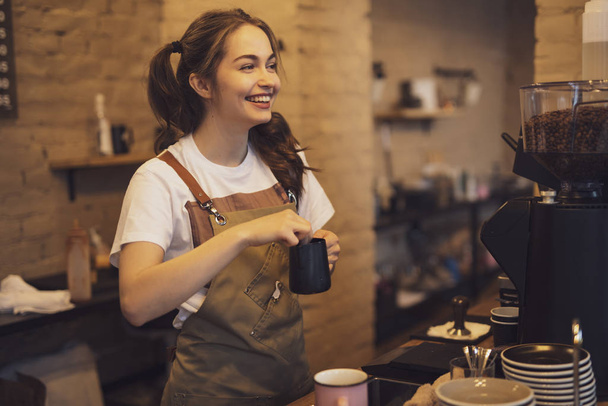 Young and cheerful barista woman make a coffee in the cafeteria - Fotoğraf, Görsel