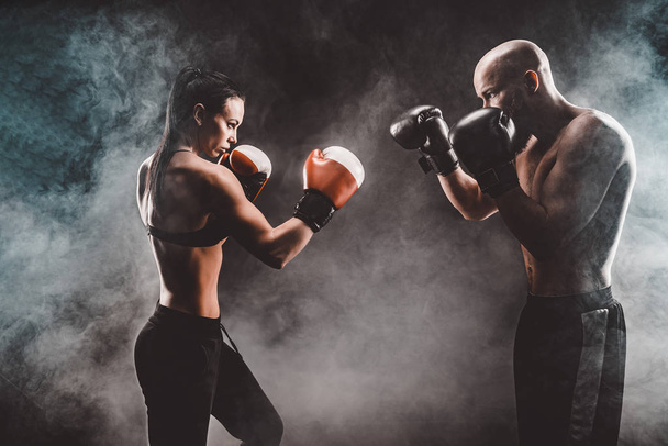 Shirtless Woman exercising with trainer at boxing and self defense lesson, studio, smoke on background. Female and male fight - Fotoğraf, Görsel