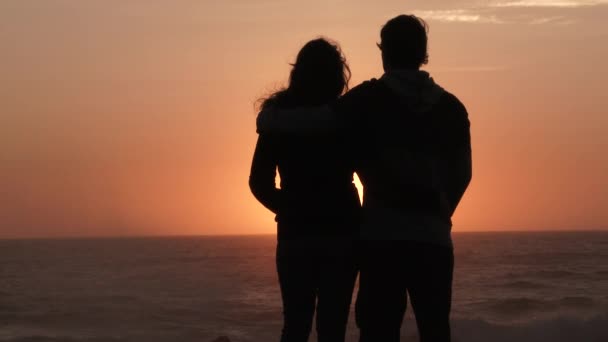 A couple in love watch the sunset and kiss at the Pacific Coast, slow motion silhouette. - Footage, Video