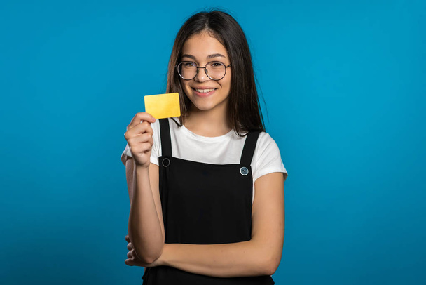 Successful pretty asian girl look to camera and showing unlimited gold credit card on blue studio background.  - Photo, Image