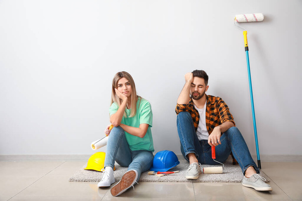 Tired young couple with tools sitting near light wall in new apartment - Foto, afbeelding