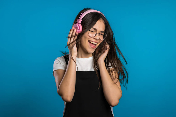 Pretty young asian girl with long hair having fun, smiling, dancing with headphones in studio against blue background. Music, dance, radio concept, - Foto, Imagem