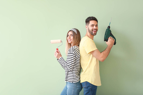 Молодая пара с краской ролика и сверла рядом с цветной стеной в новой квартире
 - Фото, изображение