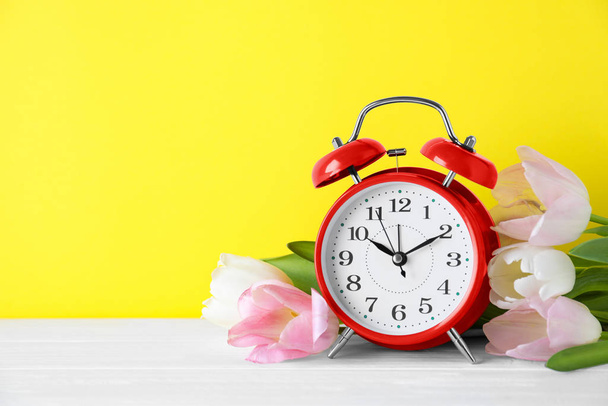 Red alarm clock and spring flowers on yellow background, space for text. Time change - Photo, image