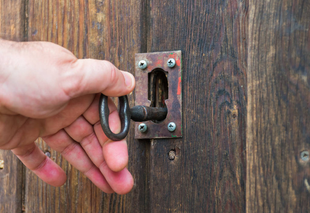 witte hand het verplaatsen van een oude of vintage sleutel gemaakt van metaal ijzer in een slot van een houten deur. De oude sleutel en het slot zijn volledig roestig en klaar om de deur te openen. Horizontale foto. - Foto, afbeelding