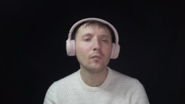 Een man luistert naar muziek in roze koptelefoon tegen een zwarte achtergrond - Video