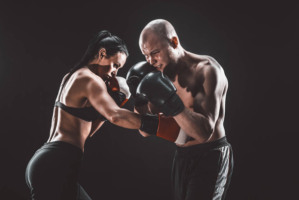 Shirtless Woman exercising with trainer at boxing and self defense lesson, studio, smoke on background. Female and male fight - Foto, afbeelding