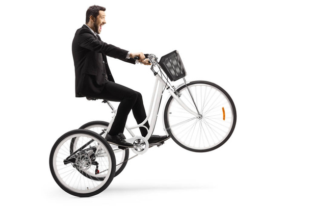 Man in a suit riding a white tricycle with front wheel up isolated on white background - Фото, изображение
