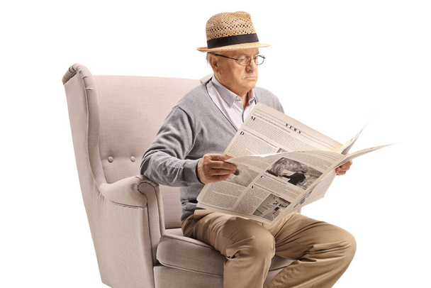 Senior man sitting in an armchair and reading a newspaper isolated on white background - Photo, Image